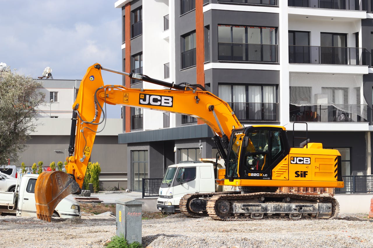 why-choose-us A yellow excavator operating at a city construction site in front of modern buildings.